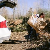 Image of woman dumping bag of leaves into pile. 