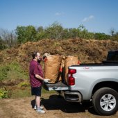 Image of person unloading bags of yard waste from a silver truck.