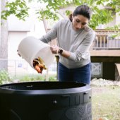 Image of woman dumping food scraps into a backyard home composter. 