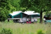 Pop-up camper situated on a campsite surrounded by trees and tall grass.
