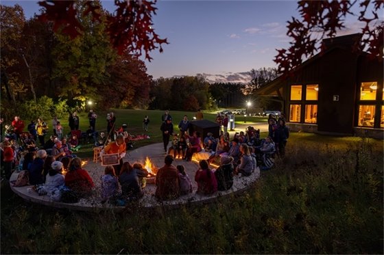 Group of people surrounding a firepit listening to a story at night. 