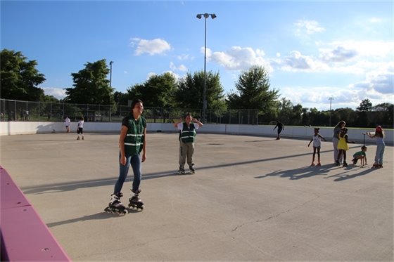 Young person on roller skates with other skaters surrounding her.