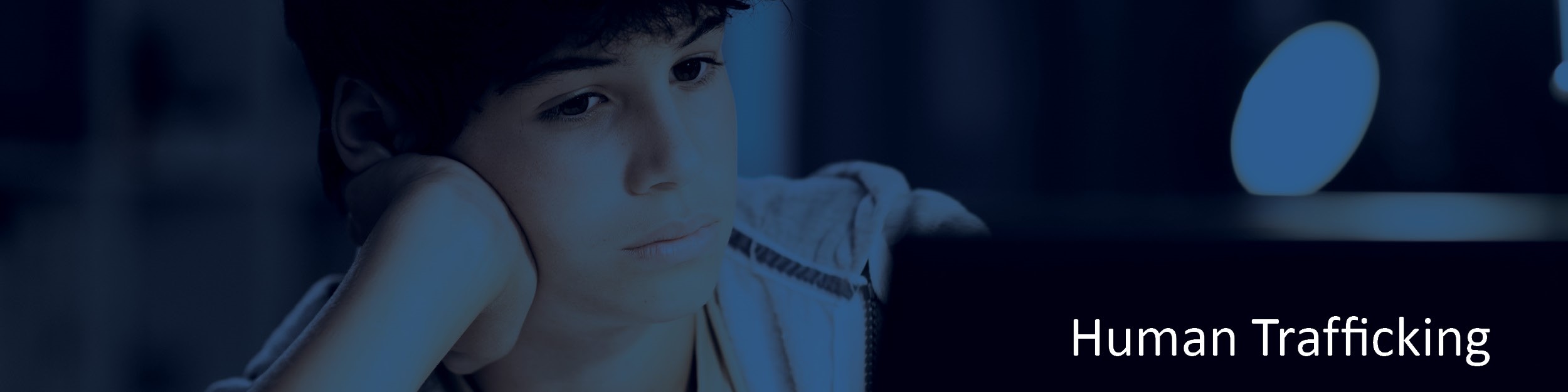 Young person staring at a monitor set against dark background with text "human trafficking"
