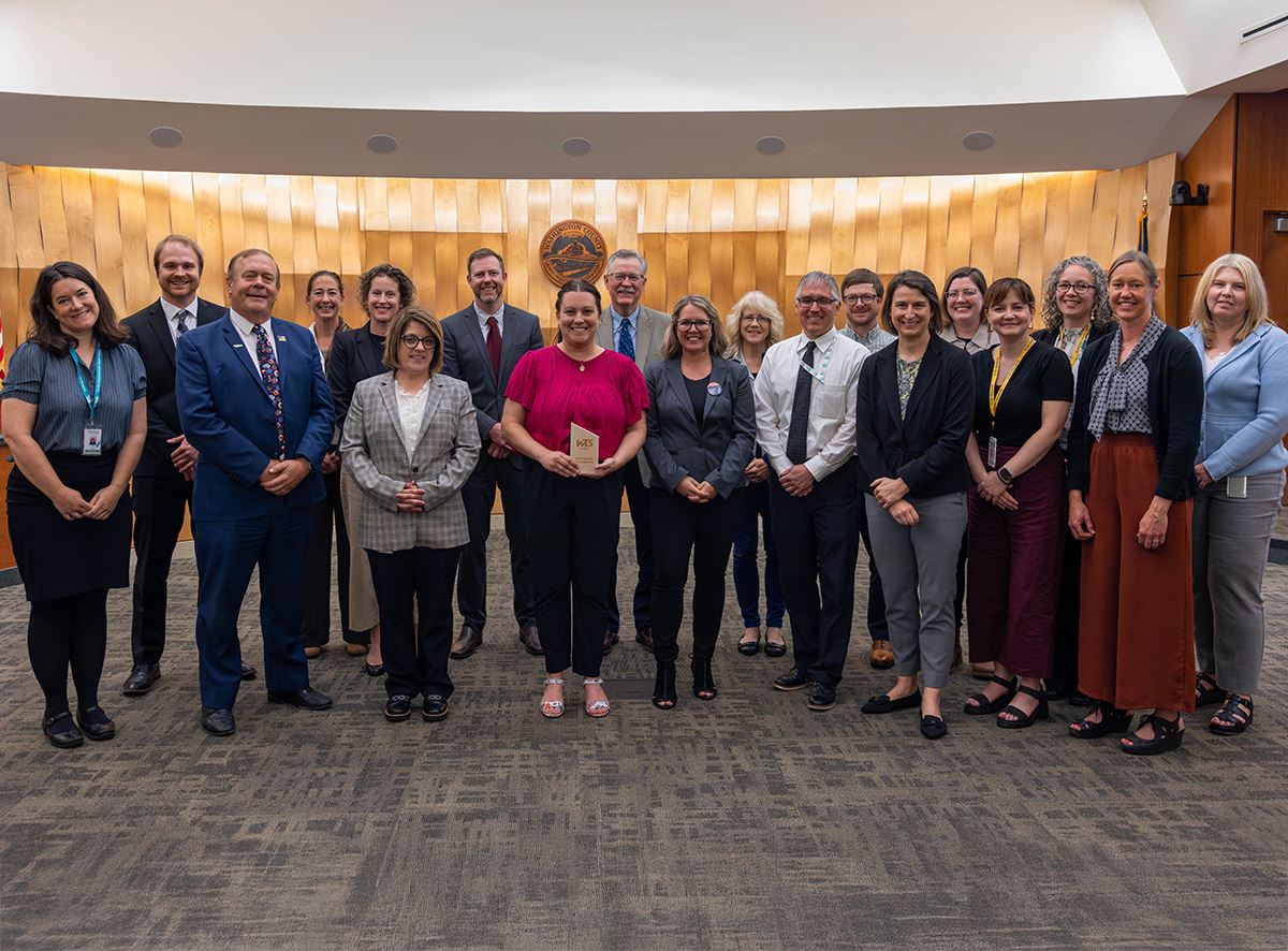 Group of staff standing in a semi-circle in the Board Meeting room.