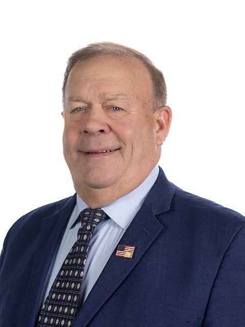 Portrait of Commissioner Karwoski in blue suit and patterned tie, with a lapel pin of the U.S. flag.